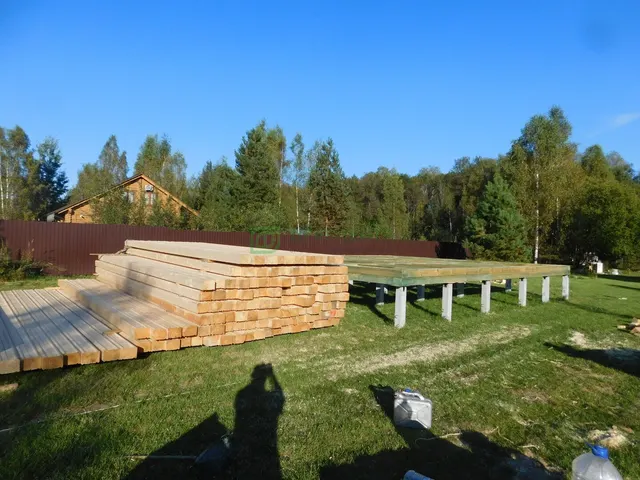 Пачки бруса рядом с обвязкой на свайном фундаменте